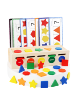 A toddler sitting on a colorful playroom rug, playing with a wooden Montessori-style shape and color sorting toy. The child is wearing blue overalls and a yellow shirt, focused on placing a green wooden square into a slot. Several colorful shapes like stars, circles, and triangles are scattered on the floor around the toy.